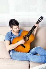 Young man with guitar on sofa in room