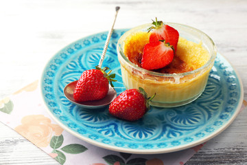 Creme brulee dessert with fresh strawberry berries on napkin, on color wooden background