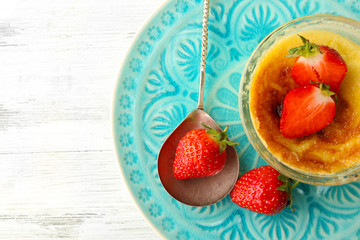Creme brulee dessert with fresh strawberry berries on napkin, on color wooden background