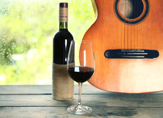 Fototapety  Gitara akustyczna i kieliszek wina przy oknie z kroplami deszczu