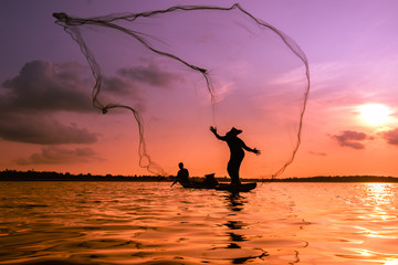 Silhouette of a fisherman throwing his net with beautiful sky.
