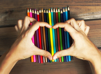 Female hands in the shape of a heart on colored pencils on a bac