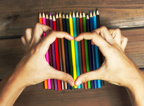 Female hands in the shape of a heart on colored pencils on a bac