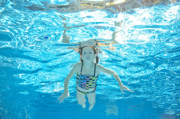 Obraz na płótnie Canvas Child swims in pool underwater, happy active girl has fun in water
