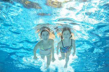 Obraz na płótnie Canvas Children swim in pool underwater, happy active girls have fun in water