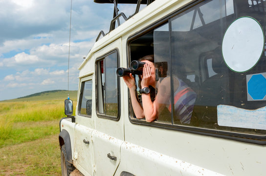 Woman tourist on safari in Africa, travel in Kenya, watching wildlife in savanna with binoculars
