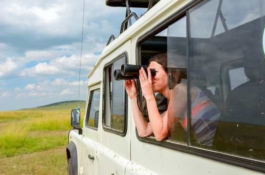 Woman tourist on safari in Africa, travel in Kenya, watching wildlife in savanna with binoculars
