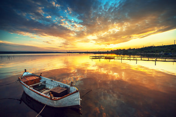Beautiful sunset over calm lake and a boat with sky reflecting i