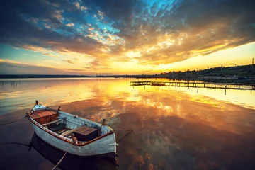 Schilderijen op glas Beautiful sunset over calm lake and a boat with sky reflecting i © ValentinValkov
