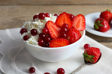 Bowl of cottage cheese with strawberry and cranberry on table, closeup