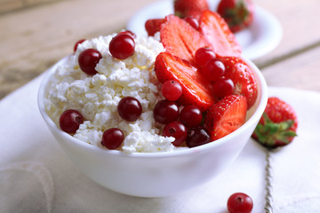 Bowl of cottage cheese with strawberry and cranberry on table, closeup