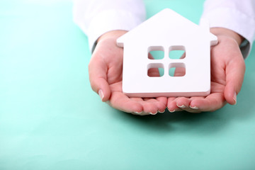 Female hands holding house on color background
