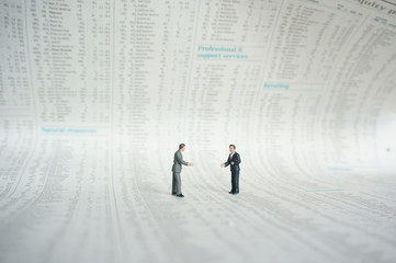 Miniature business figures newspaper.
Miniature scale model businessmen standing on shares page of a newspaper.