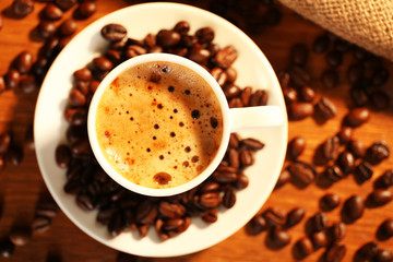 Cup of fresh coffee with beans on table, closeup