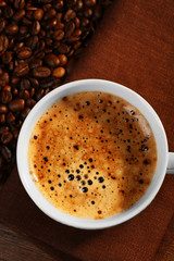 Cup of fresh coffee with beans on table, closeup