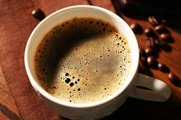 Cup of fresh coffee with beans on table, closeup