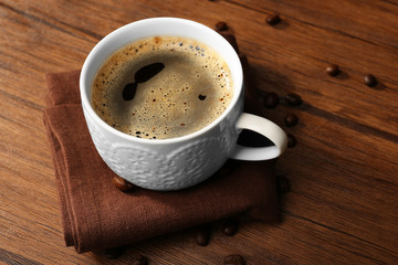 Cup of fresh coffee with beans on table, closeup