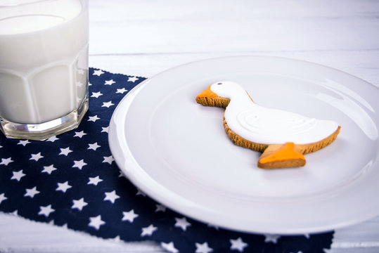 Cup of milk and ginger duckshape cookies on a white wooden table and dark blue naplin with stars.