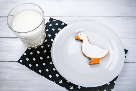 Cup of milk and ginger duckshape cookies on a white wooden table and dark blue naplin with stars.