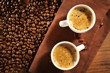 Two cups of fresh coffee with beans on table, top view