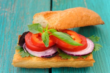 Sandwich with red onion, tomatoes and basil on blue wooden table