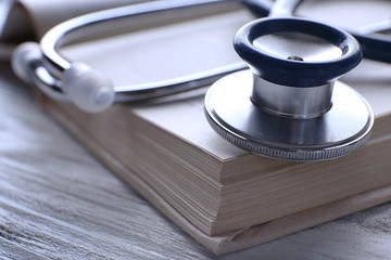 Stethoscope on book on wooden table, closeup