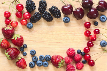 Frame from fresh berries laid around on the wooden plate