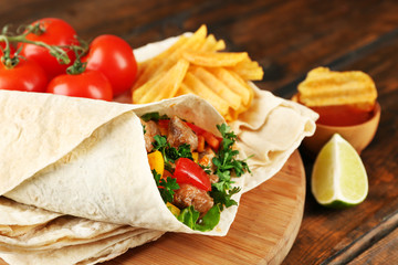 Homemade tasty burrito with vegetables and potato chips on cutting board, on wooden background