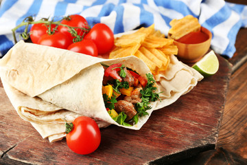 Homemade tasty burrito with vegetables and potato chips on cutting board, on wooden background