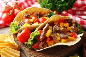 Homemade tasty burrito with vegetables and potato chips on cutting board, on wooden background