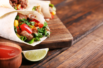 Homemade tasty burrito with vegetables on cutting board, on wooden background