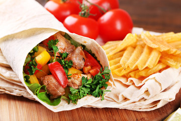 Homemade tasty burrito with vegetables and potato chips on cutting board, on wooden background