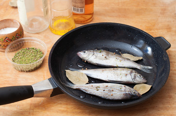 Fresh fishes with spices on a frying pan on wooden background