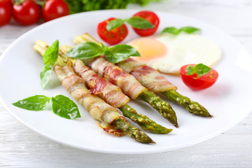 Dish of asparagus with bacon and egg in plate on table, closeup