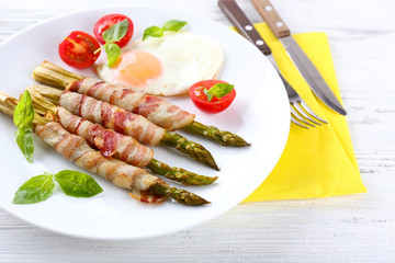 Dish of asparagus with bacon and egg in plate on table, closeup