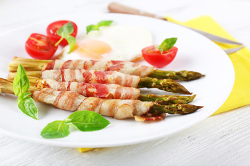 Dish of asparagus with bacon and egg in plate on table, closeup