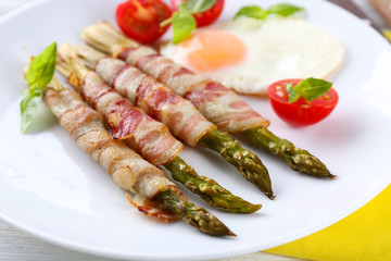 Dish of asparagus with bacon and egg in plate on table, closeup