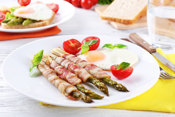 Dish of asparagus with bacon and egg in plate on table, closeup