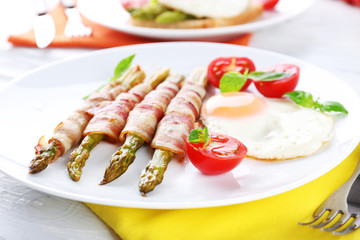 Dish of asparagus with bacon and egg in plate on table, closeup