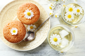 Obraz na płótnie Canvas Glasses of chamomile tea with chamomile flowers and tasty muffins on color wooden background