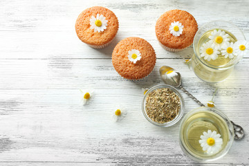 Fototapeta na wymiar Glasses of chamomile tea with chamomile flowers and tasty muffins on color wooden background