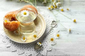 Glass of chamomile tea with chamomile flowers and tasty muffins on color wooden background