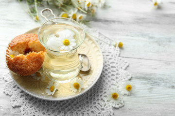 Glass of chamomile tea with chamomile flowers and tasty muffins on color wooden background