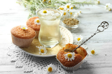 Glass of chamomile tea with chamomile flowers and tasty muffins on color wooden background