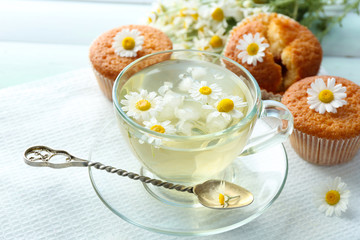 Cup of chamomile tea with chamomile flowers and tasty muffins on color wooden background