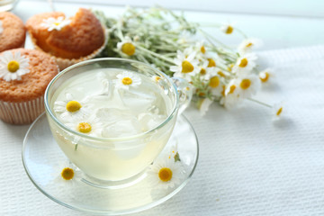 Cup of chamomile tea with chamomile flowers and tasty muffins on color wooden background