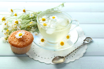 Cup of chamomile tea with chamomile flowers and tasty muffin on color wooden background