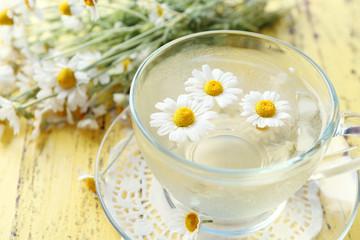 Obraz na płótnie Canvas Glass of cold chamomile tea with ice cubes and chamomile flowers on color wooden background