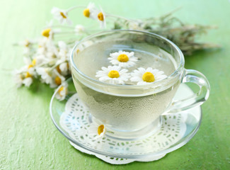 Obraz na płótnie Canvas Glass of cold chamomile tea with ice cubes and chamomile flowers on color wooden background
