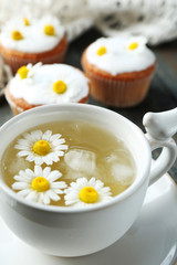 Cup of chamomile tea with chamomile flowers and tasty muffins  on color wooden background